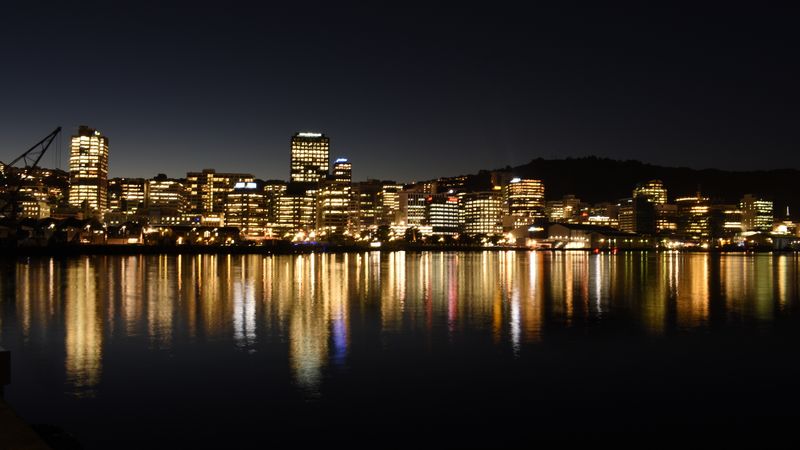 City skyline reflected in dark harbor water, illuminated at night